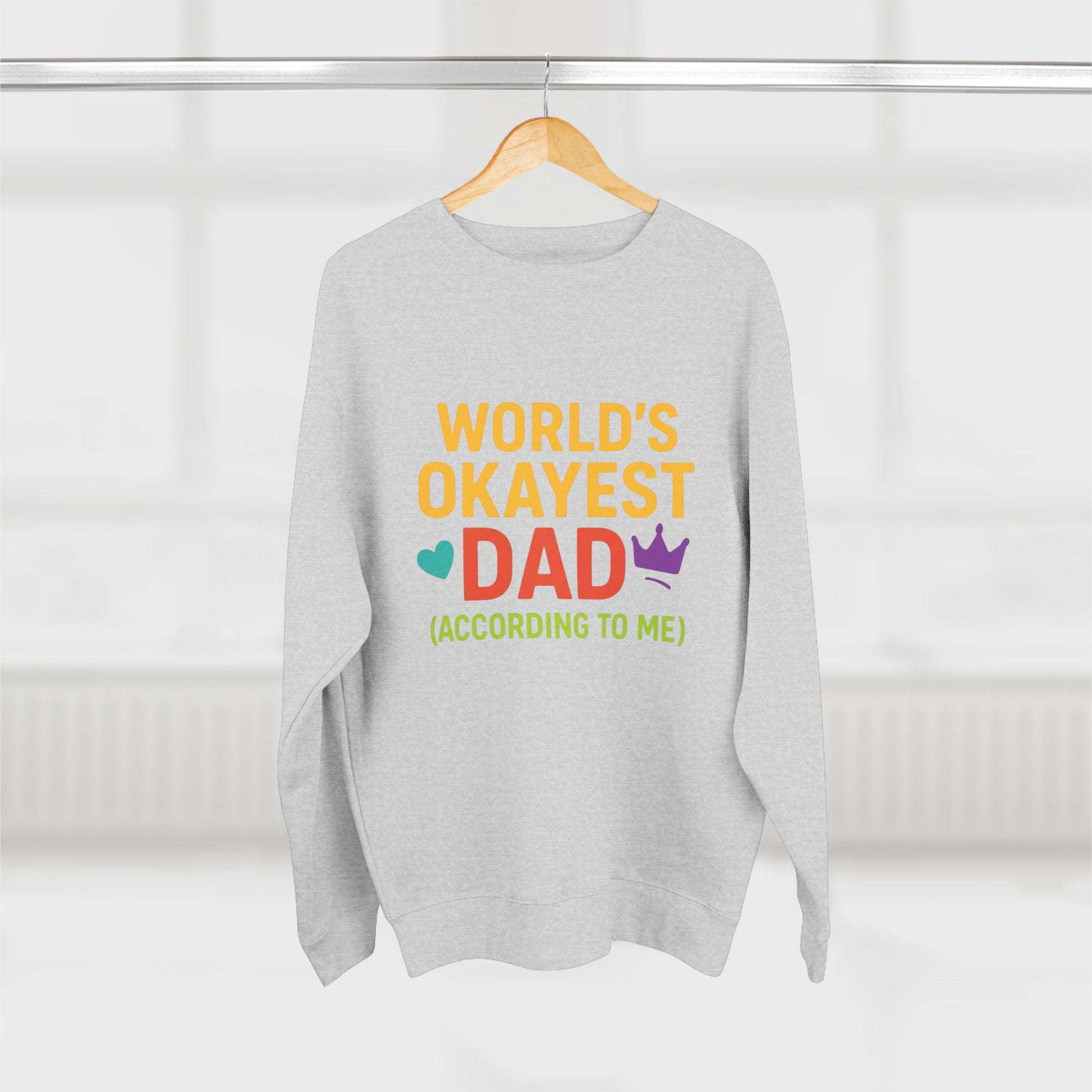 Gray sweatshirt with colorful text 'World's Okayest Dad (According to Me)' on a hanger against a white background