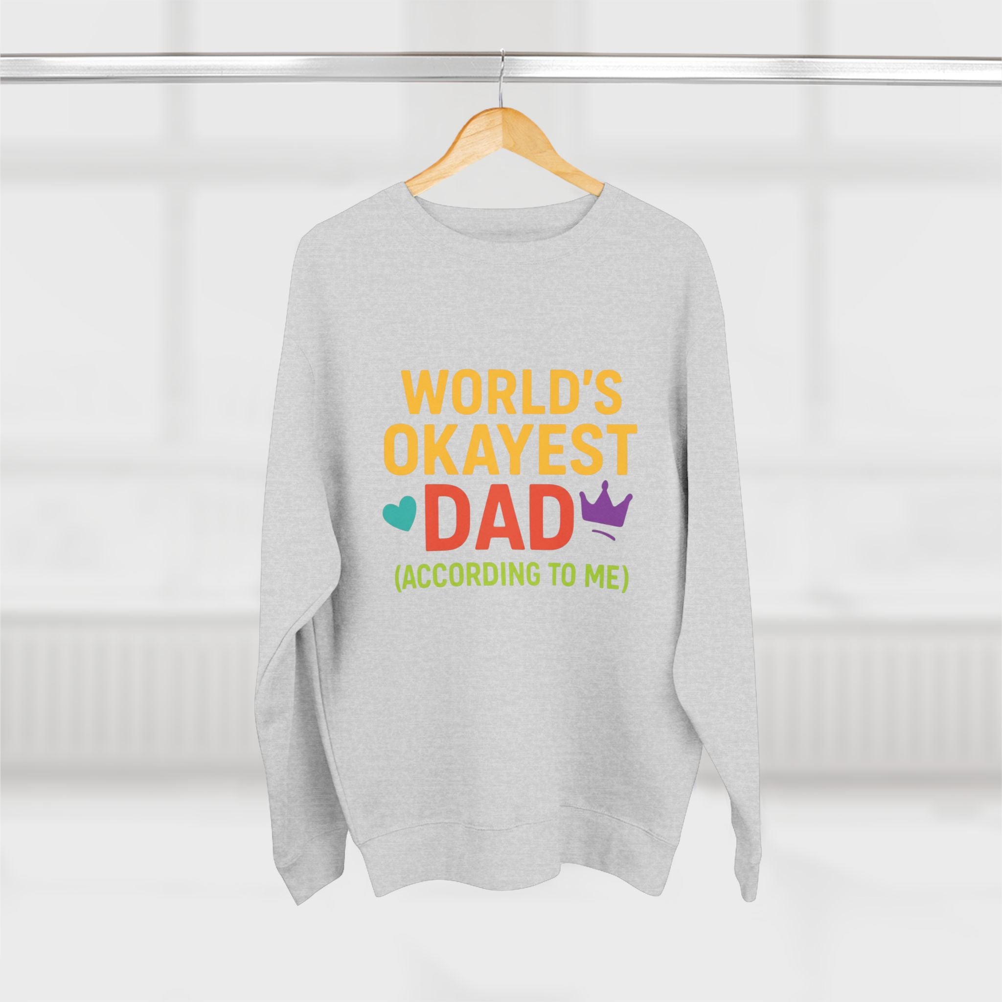 Gray sweatshirt with colorful text 'World's Okayest Dad (According to Me)' on a hanger against a white background