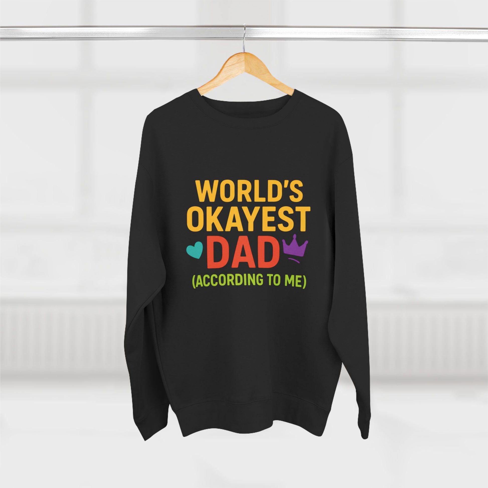 Black sweatshirt with colorful text 'World's Okayest Dad' on a hanger against a white background