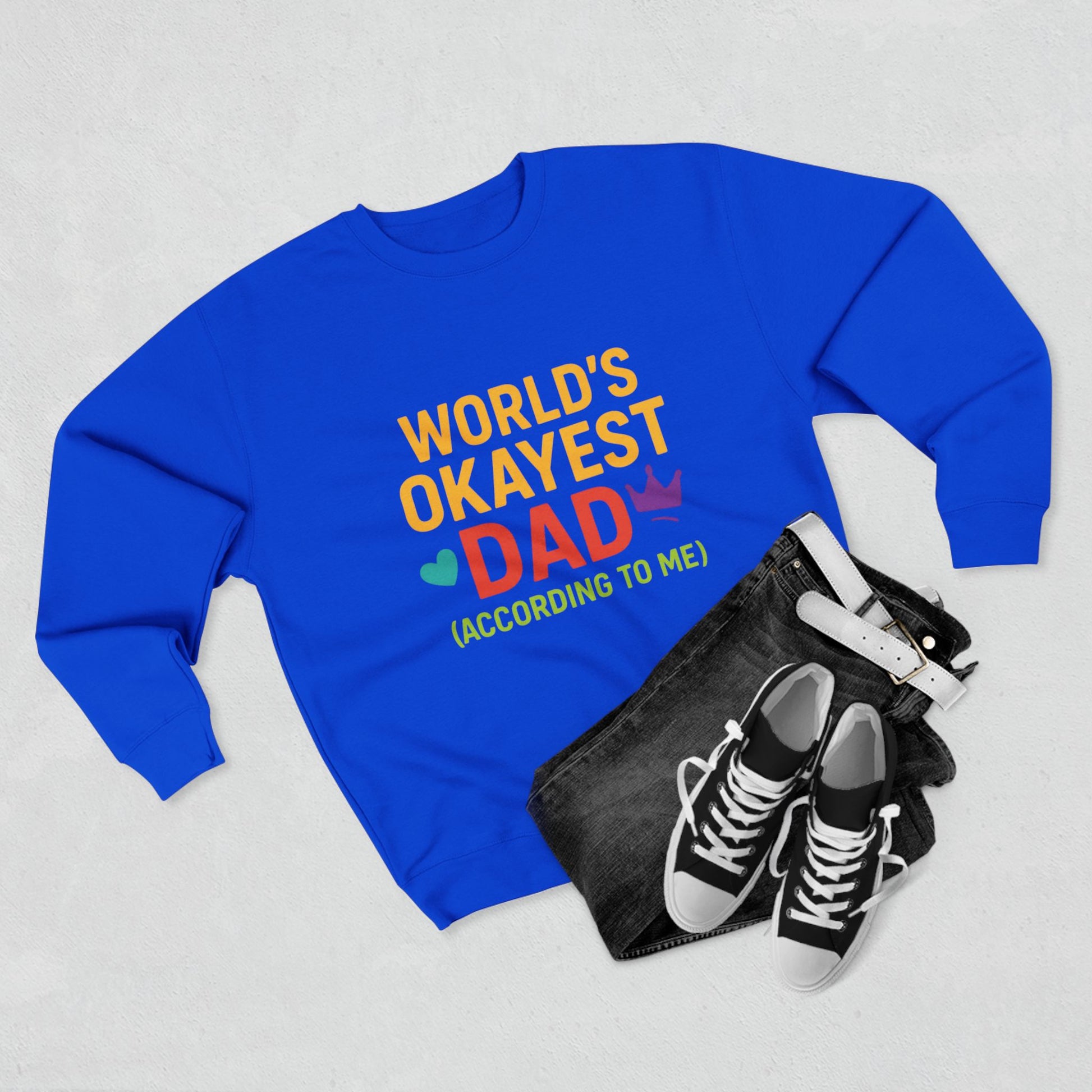 Blue sweatshirt with 'World's Okayest Dad' text, black sneakers, and pouch on a light gray background